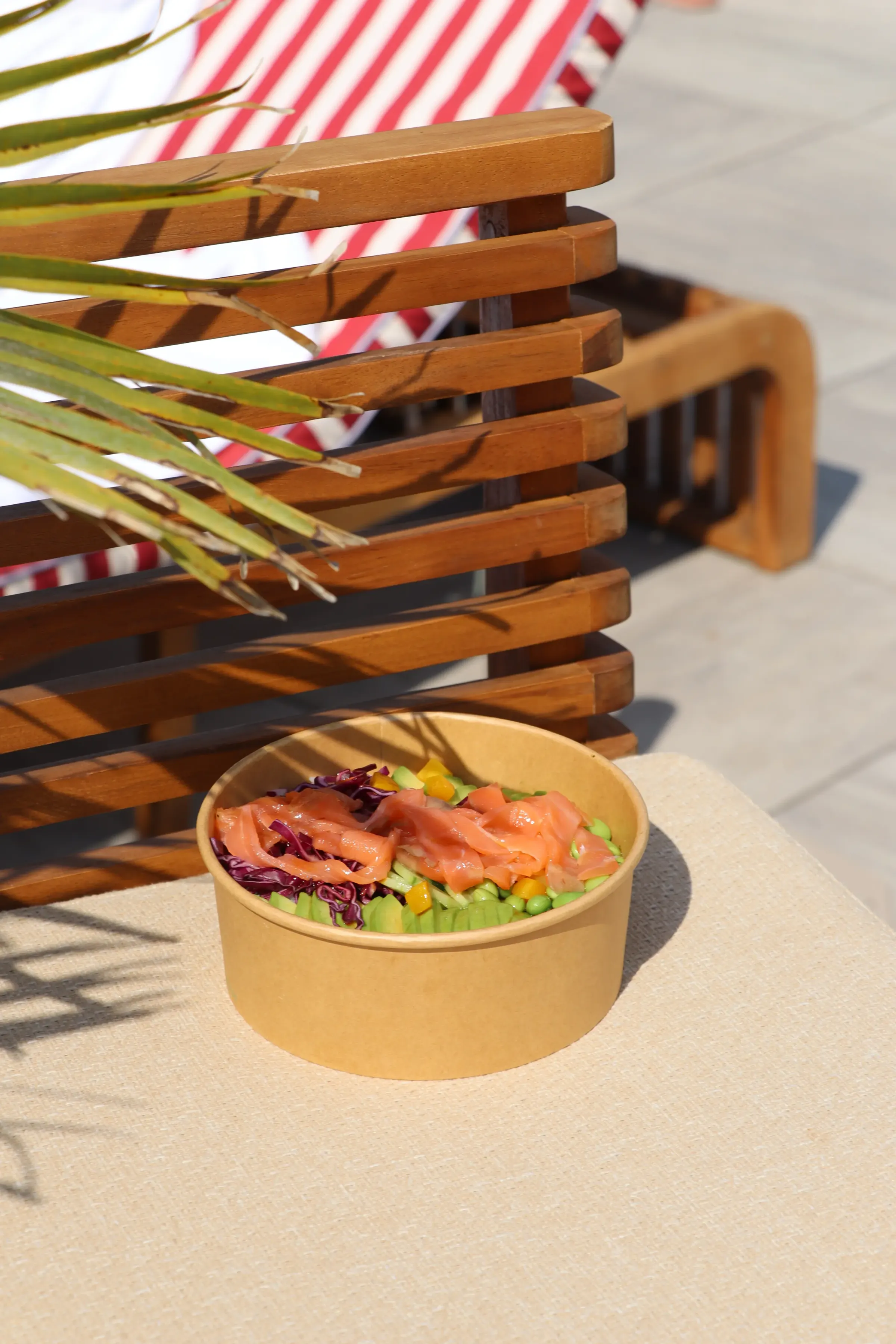 Un bol de salade contenant des dés de tomates, de concombres et de chou rouge posé sur une chaise en bois près d'une table à rayures rouges et blanches