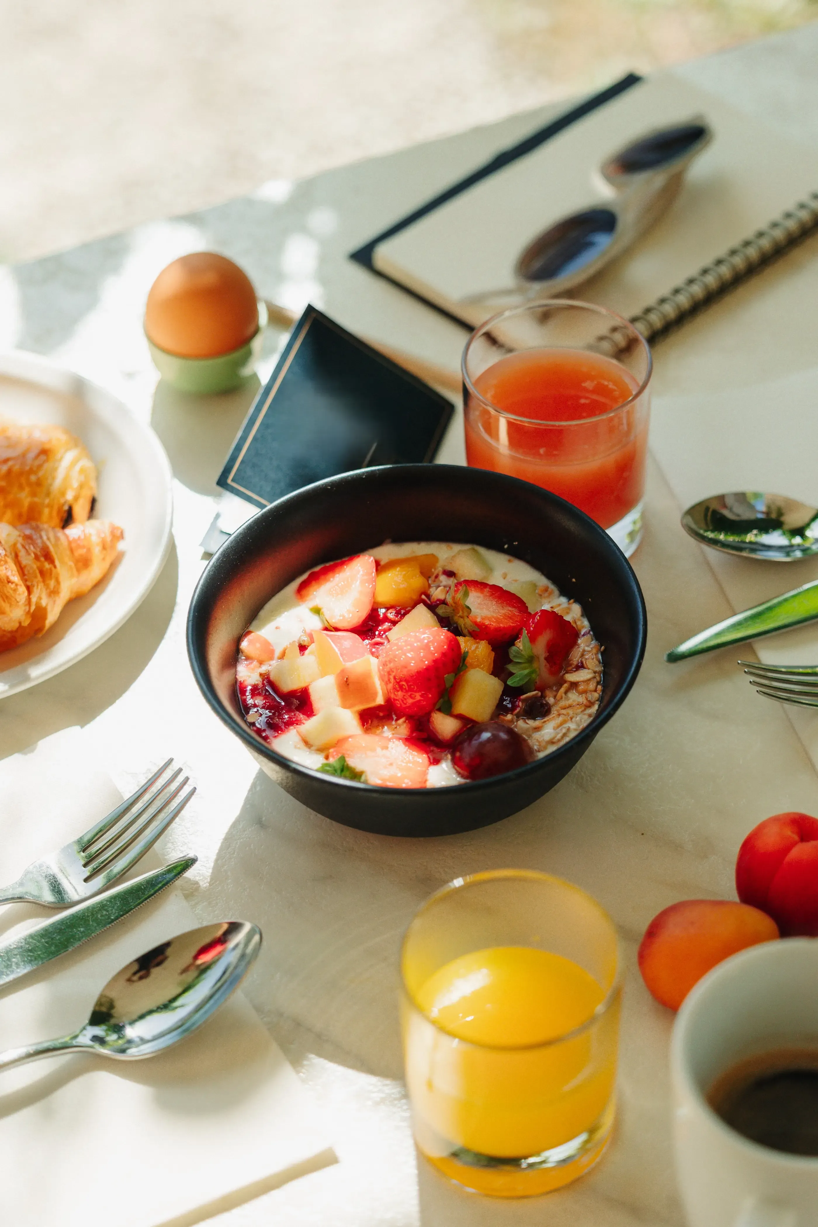 Un bol de porridge aux fruits frais, des croissants, des verres de jus, des œufs et des couverts sur une table